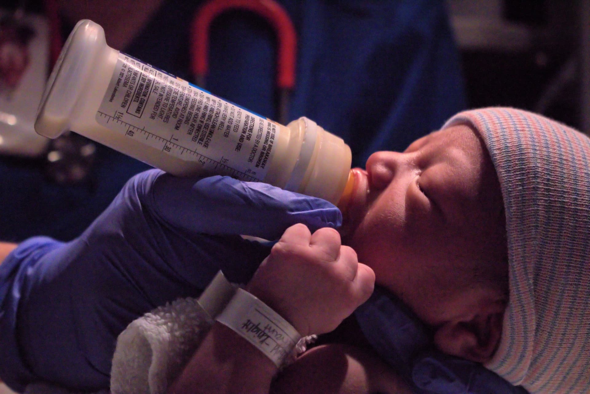 A newborn being fed from a bottle, held in a gloved hand (illustrative photo)