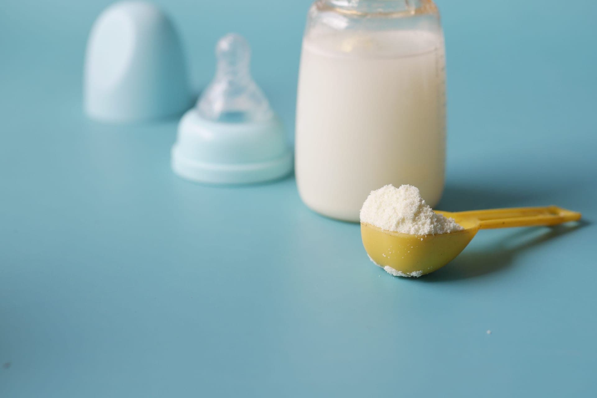 Close-up of powdered infant formula in a scoop beside a baby bottle (illustrative photo)